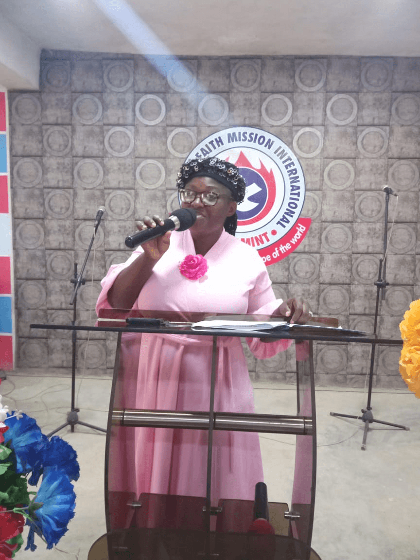 A woman in pink speaking into a microphone from a lectern.