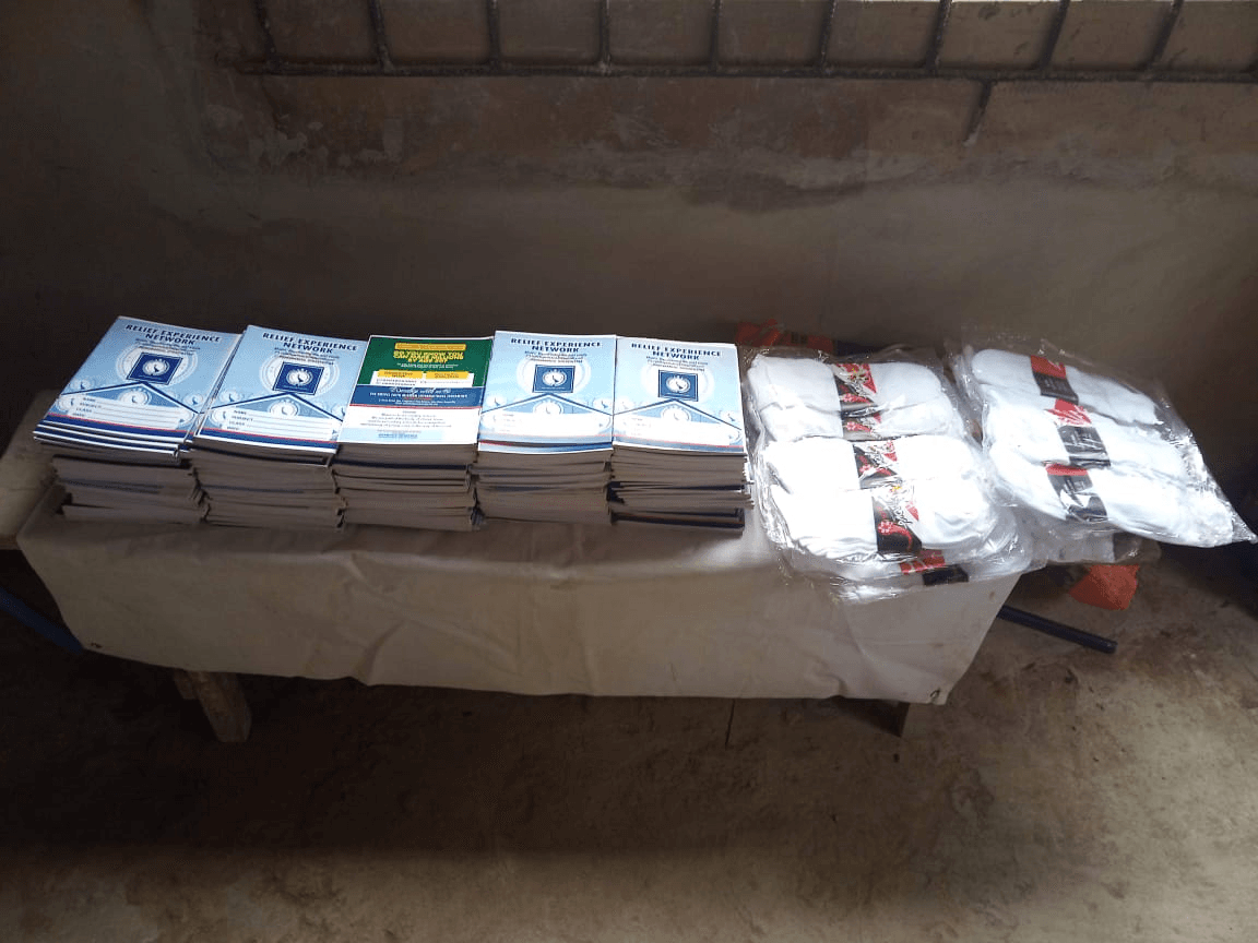 Exercise books branded Relief Experience Network stacked in piles on a cloth-covered table, with packs of white socks beside them.