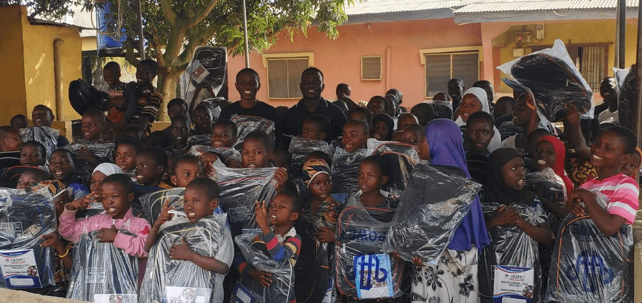 Children packed close together, grinning and holding up their new school bags.